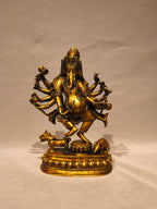 A golden brass statue of Lord Ganesha, the Hindu deity representing wisdom and discipline, standing on a decorated pedestal with a cow and elephant at his base, set against a neutral beige background.