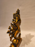 A small metallic gold statue of Lord Ganesha standing on a decorated base, photographed against a plain light background with a soft shadow.