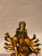 A golden brass statue of a multi-armed Ganesha figure, photographed against a plain light beige background.