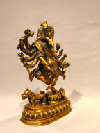 A golden brass statue of Lord Ganesha, the Hindu deity representing wisdom and discipline, standing on a decorated pedestal with a small animal at the front, set against a plain light background.